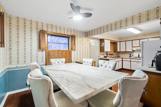 dining space featuring brick floor, wallpapered walls, and a ceiling fan