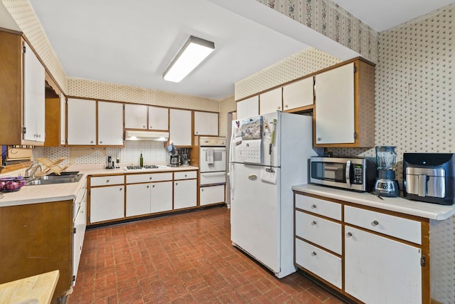 kitchen with brick floor, wallpapered walls, white appliances, and under cabinet range hood