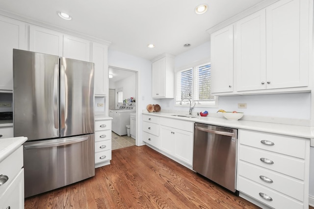 kitchen with washer and clothes dryer, light countertops, white cabinets, a sink, and appliances with stainless steel finishes