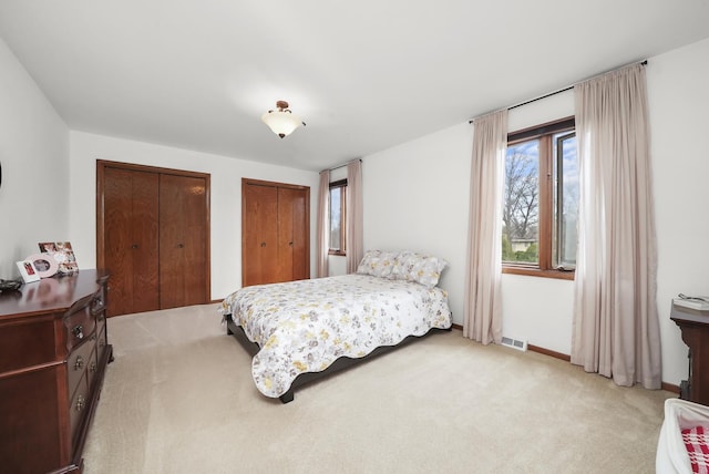 bedroom featuring two closets, light colored carpet, baseboards, and visible vents