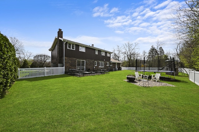 rear view of house with a fenced backyard, a chimney, brick siding, a lawn, and a trampoline
