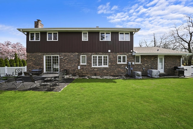 rear view of house with a yard, brick siding, a chimney, and a patio area