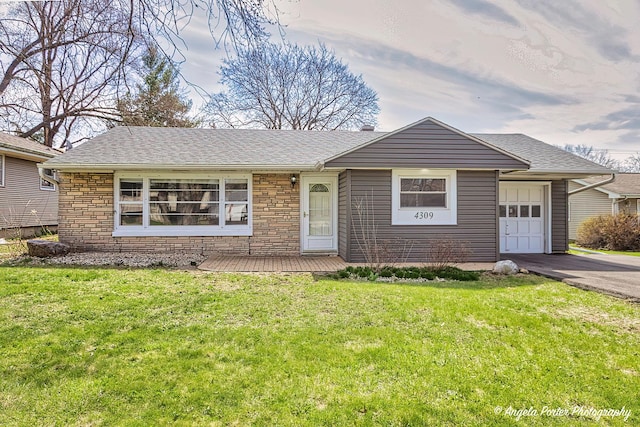 ranch-style home with a front yard, stone siding, a garage, driveway, and roof with shingles