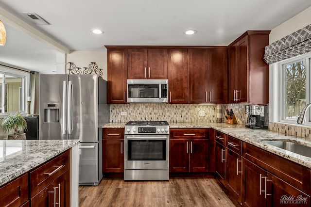 kitchen with tasteful backsplash, visible vents, appliances with stainless steel finishes, a sink, and reddish brown cabinets