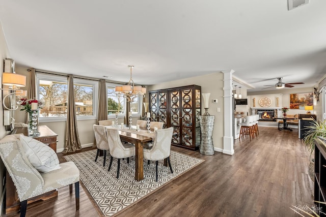 dining area featuring ceiling fan with notable chandelier, visible vents, dark wood-style floors, and a glass covered fireplace