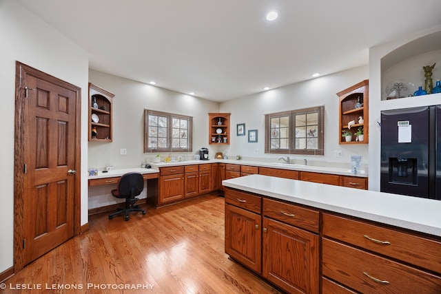 kitchen with light countertops, open shelves, black refrigerator with ice dispenser, light wood-style floors, and a sink