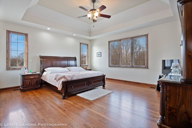 bedroom featuring light wood-style flooring, a tray ceiling, baseboards, and recessed lighting