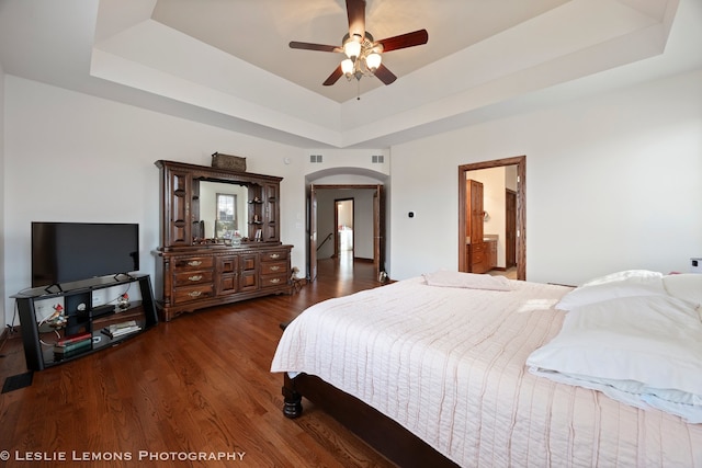 bedroom featuring a tray ceiling, arched walkways, wood finished floors, and visible vents