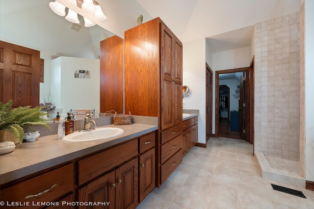full bath featuring tile patterned floors, tiled shower, vanity, and lofted ceiling