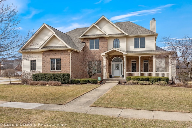 view of front facade featuring a porch, brick siding, a shingled roof, and a front yard