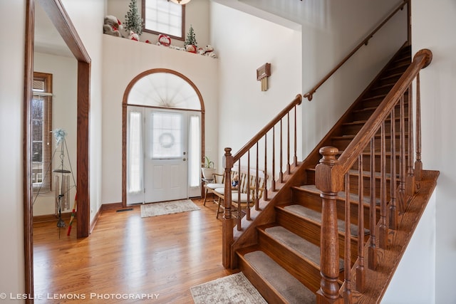 foyer entrance featuring visible vents, baseboards, a towering ceiling, wood finished floors, and stairs