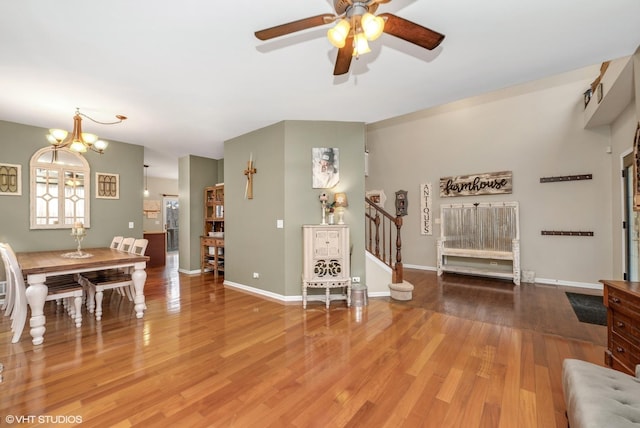 living area with baseboards, stairway, wood finished floors, and ceiling fan with notable chandelier