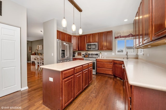 kitchen with dark wood-style flooring, light countertops, stainless steel appliances, a sink, and hanging light fixtures