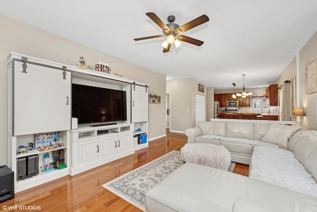 living room with a barn door, ceiling fan with notable chandelier, baseboards, and wood finished floors