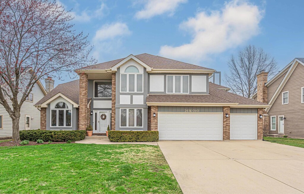 26W010 Macarthur Ave, Carol Stream, IL 60188 - view of front facade featuring a shingled roof, concrete driveway, stucco siding, brick siding, and a front lawn