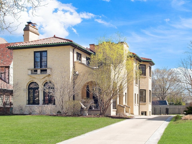 view of property exterior with a tiled roof, driveway, a chimney, brick siding, and a balcony