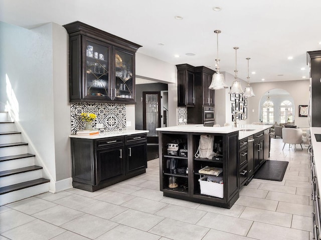 kitchen with arched walkways, a sink, dark cabinetry, light countertops, and recessed lighting
