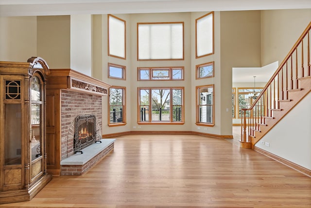 unfurnished living room with stairs, baseboards, a brick fireplace, and wood finished floors