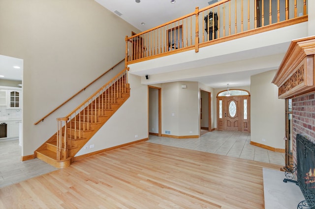 unfurnished living room featuring a brick fireplace, wood finished floors, stairway, baseboards, and a high ceiling