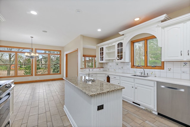 kitchen with decorative backsplash, a kitchen island, appliances with stainless steel finishes, a sink, and an inviting chandelier