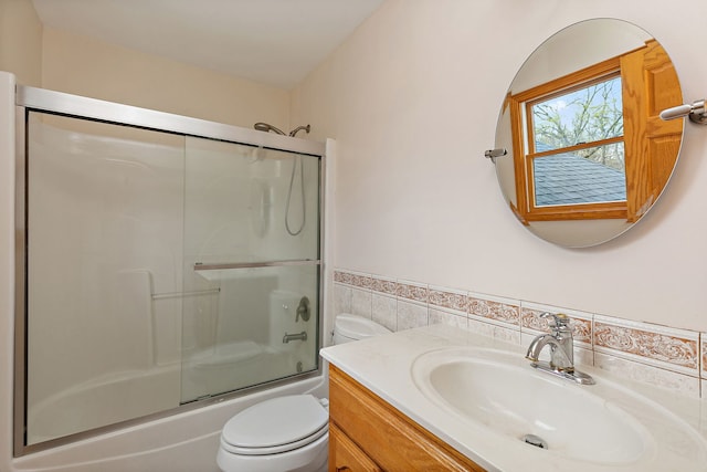 full bath featuring vanity, wainscoting, toilet, tile walls, and bath / shower combo with glass door