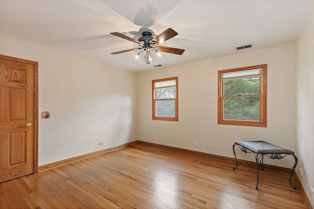 empty room with visible vents, a ceiling fan, light wood finished floors, and baseboards