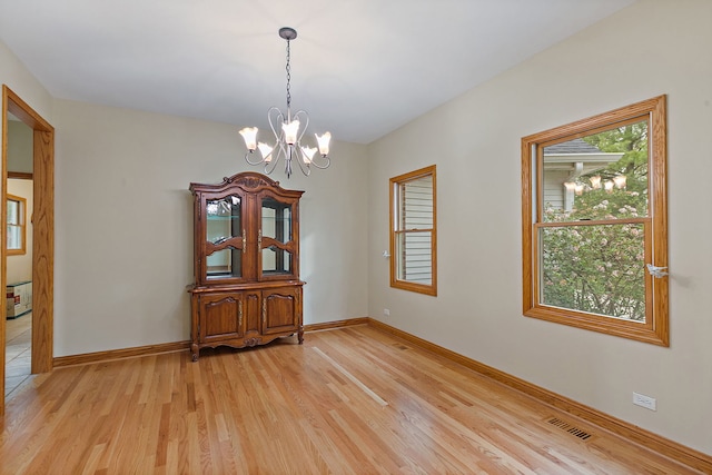 unfurnished room with a chandelier, baseboards, visible vents, and light wood-style flooring