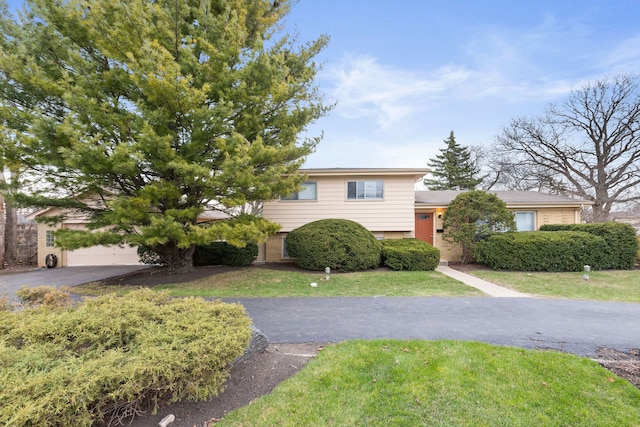 tri-level home featuring driveway, a garage, a front lawn, and brick siding