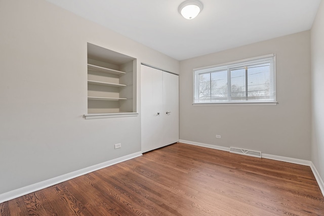 unfurnished bedroom with a closet, visible vents, baseboards, and wood finished floors