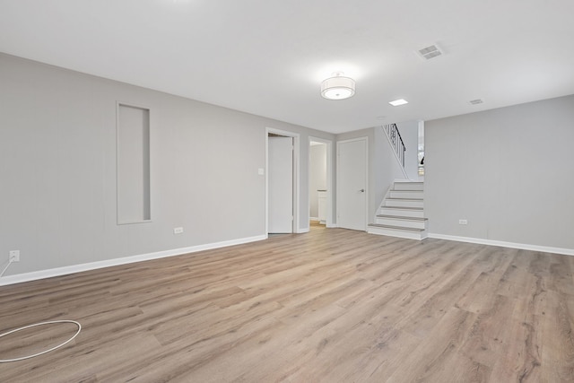 unfurnished living room with light wood-type flooring, baseboards, visible vents, and stairs