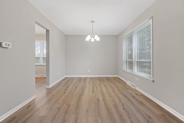 unfurnished dining area with light wood-style flooring, visible vents, baseboards, and a notable chandelier