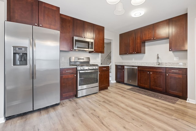 kitchen featuring stainless steel appliances, light stone countertops, light wood-type flooring, and a sink