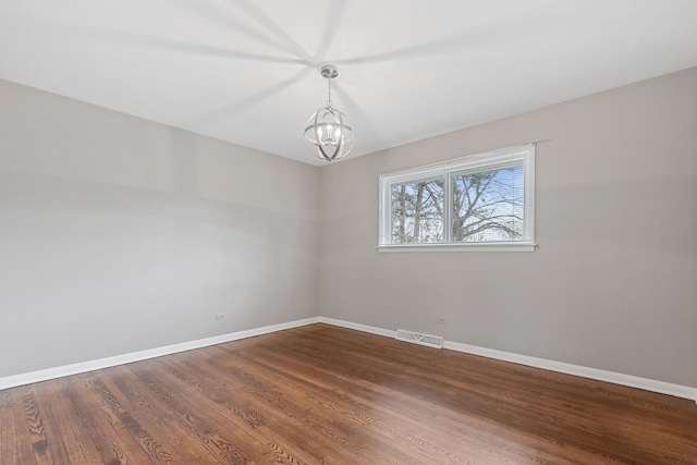 empty room featuring a chandelier, visible vents, baseboards, and dark wood finished floors