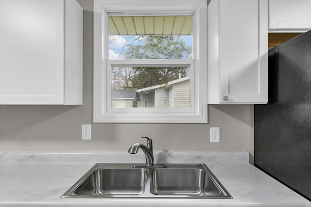 kitchen with a sink, freestanding refrigerator, and white cabinetry