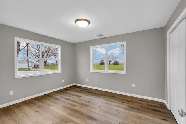 unfurnished bedroom with visible vents, multiple windows, baseboards, and wood finished floors