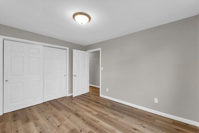 unfurnished bedroom featuring wood finished floors, baseboards, and a closet