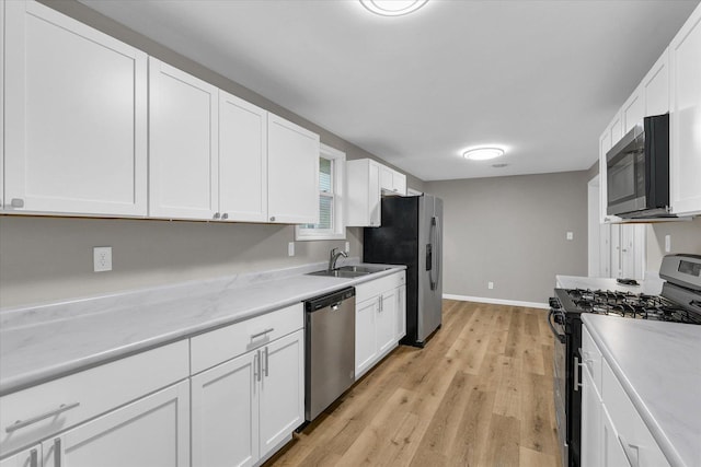 kitchen with stainless steel appliances, light wood finished floors, baseboards, and white cabinetry