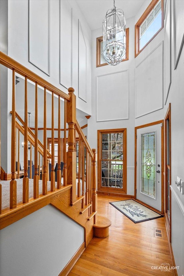 entryway featuring stairway, a towering ceiling, an inviting chandelier, wood finished floors, and visible vents