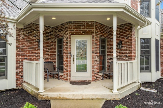view of exterior entry featuring brick siding, a porch, and a shingled roof