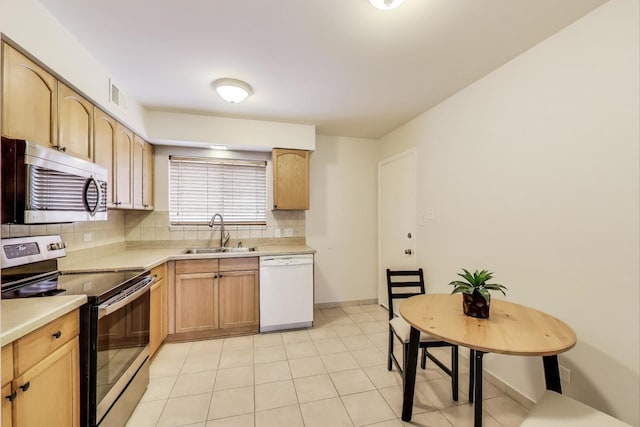 kitchen with appliances with stainless steel finishes, tasteful backsplash, a sink, and light countertops