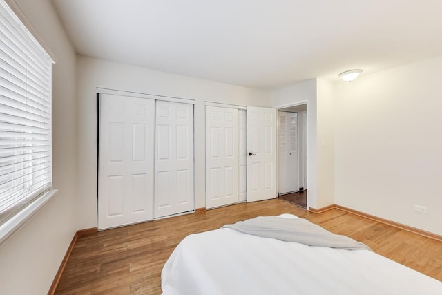 bedroom with light wood-style floors, two closets, and baseboards