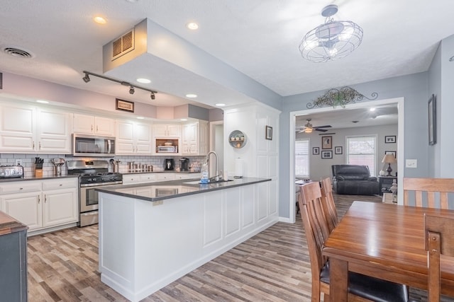 kitchen with light wood finished floors, stainless steel appliances, a sink, dark countertops, and visible vents