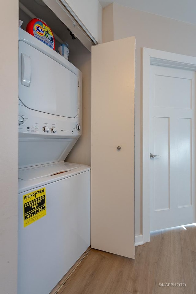 clothes washing area featuring stacked washer / dryer, laundry area, and light wood finished floors