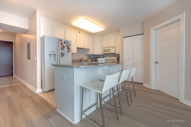 kitchen featuring white appliances, a kitchen breakfast bar, light wood-style floors, white cabinetry, and stone countertops