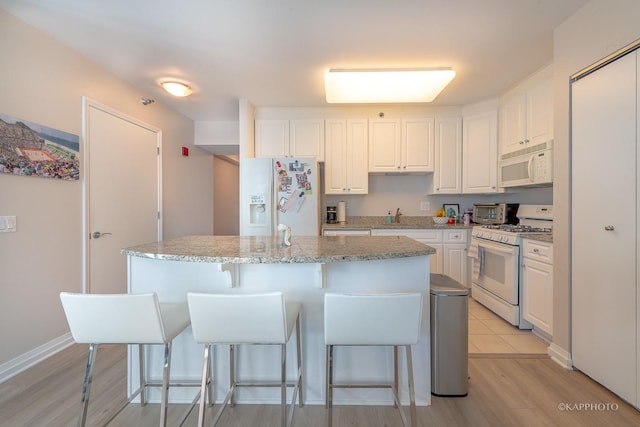 kitchen with a sink, a breakfast bar, white appliances, white cabinetry, and a kitchen island