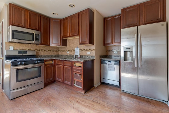 kitchen with light wood-style floors, dark stone countertops, a sink, stainless steel appliances, and decorative backsplash