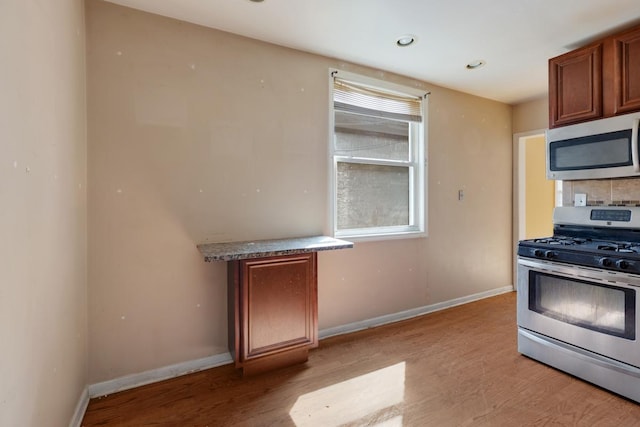 kitchen with baseboards, light wood-style flooring, backsplash, brown cabinets, and appliances with stainless steel finishes