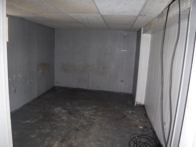 spare room with wooden walls, a drop ceiling, and unfinished concrete flooring