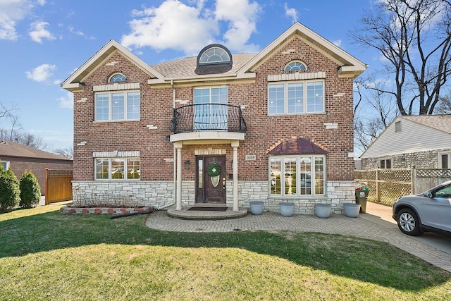 traditional-style house featuring fence, a front lawn, a balcony, brick siding, and driveway