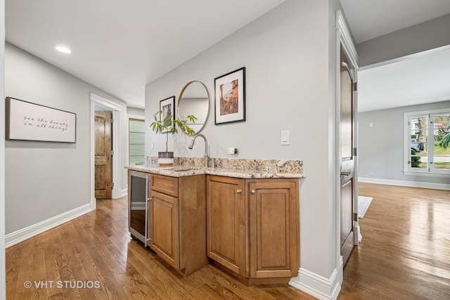 kitchen with wine cooler, light stone counters, brown cabinets, and wood finished floors